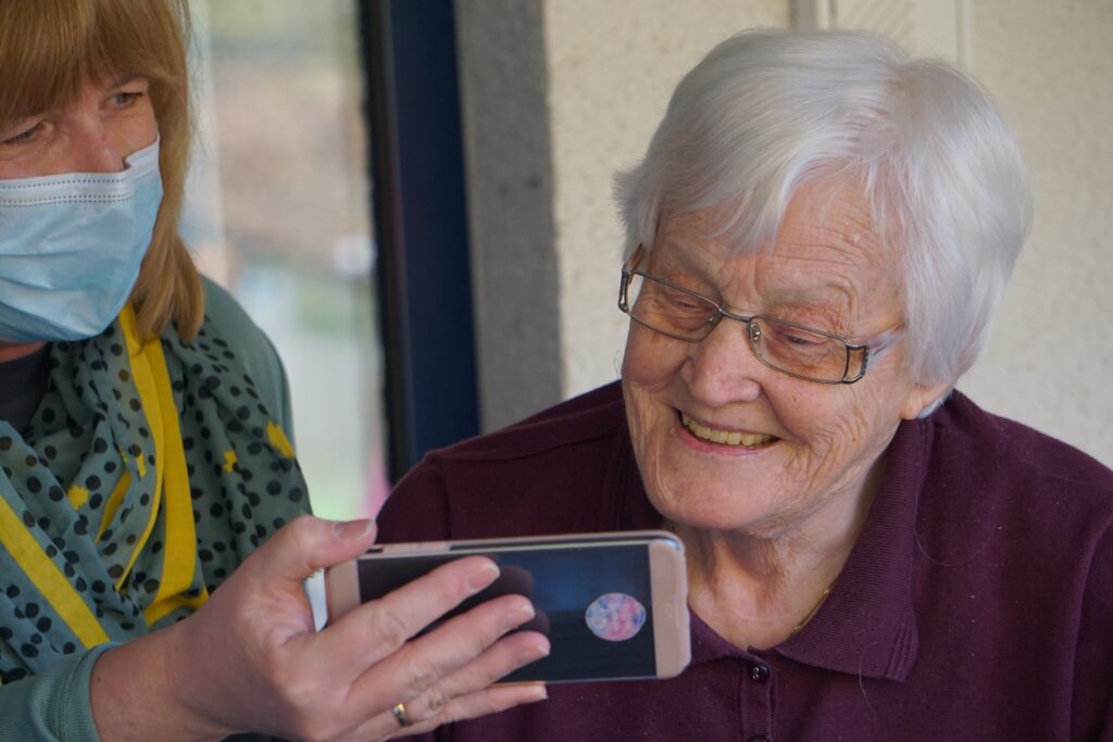 Elderly woman looking at carer's phone.