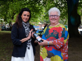 Two women stand smiling holding a an expensive bottle of single malt whisky