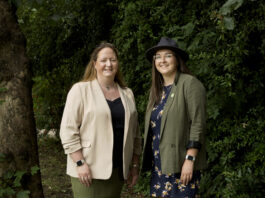 Two women smile as they pose in farming clothes and wellies