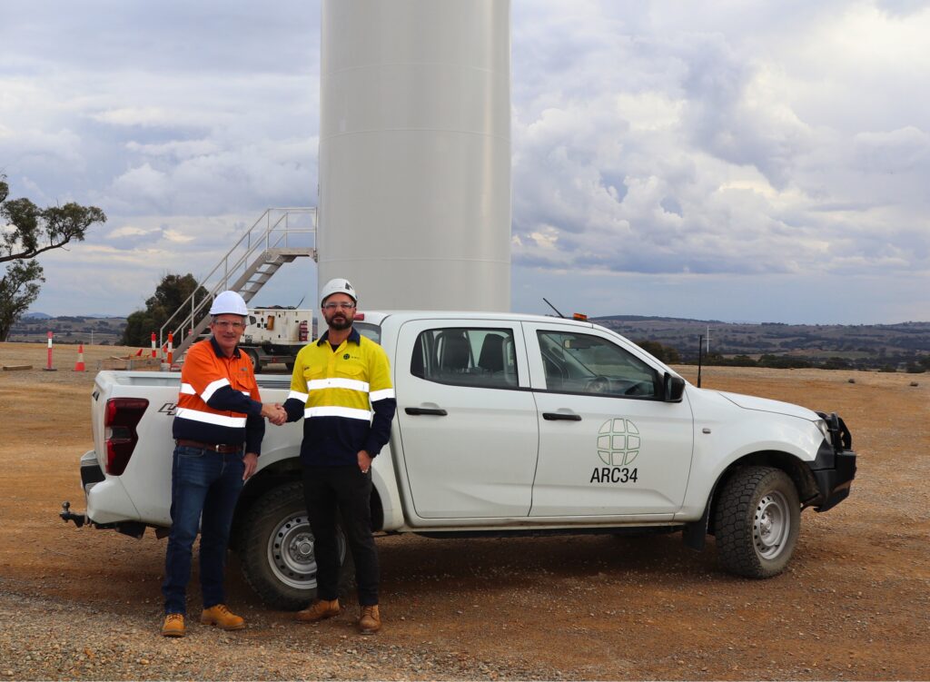 Niall Conlon and Andrew Lindsell shake hands beneath wind turbine. Image supplied with release by Aurora