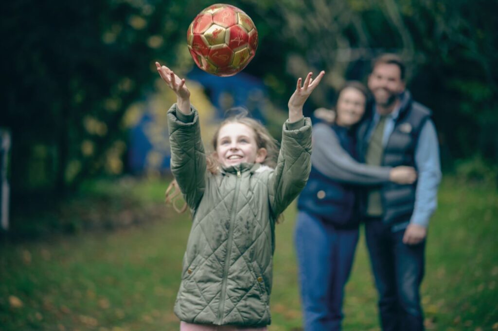 Little girl throws a ball whilst her parent watch on in the background. Image supplied with release by Bernardo's Scotland