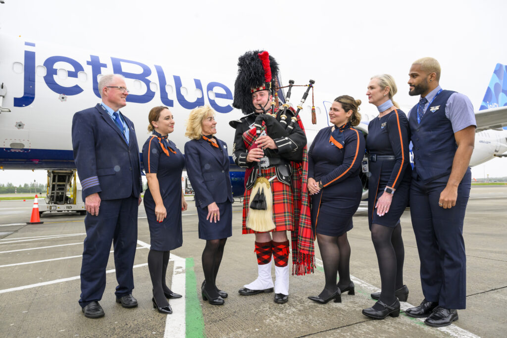 Man playing bagpipes next to JetBlue staff in front of JetBlue plane.