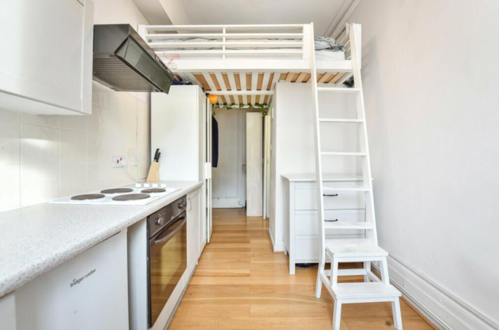 The narrow main room of the tiny apartment, with the kitchen area taking up the entire left side, and the sleeping area suspended above, accessed by a ladder.