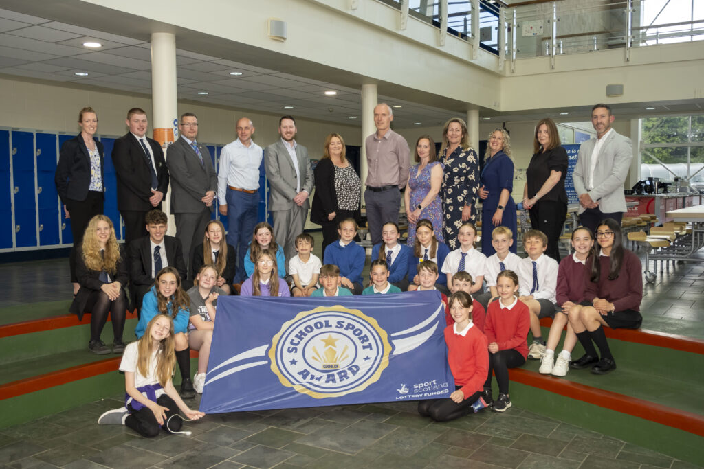 Balfron Schools Cluster students and faculty in front of award banner.