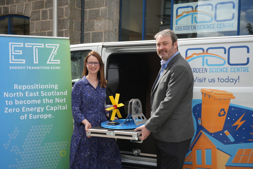 Lauren Braidwood and Brian Snelling stand in front of Aberdeen Science Centre next to an Energy Transition Zone banner, holding up the mobile wind turbine exhibit.