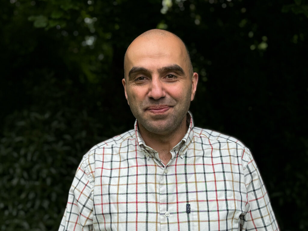 A picture of Professor Husam AlWaer, wearing a white checked shirt.