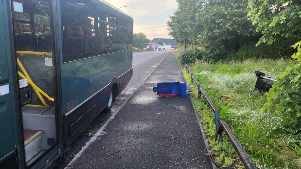 A dark green minibus parked on a deserted street. A blue seat, apparently from inside the bus, lies on the pavement alongside it.