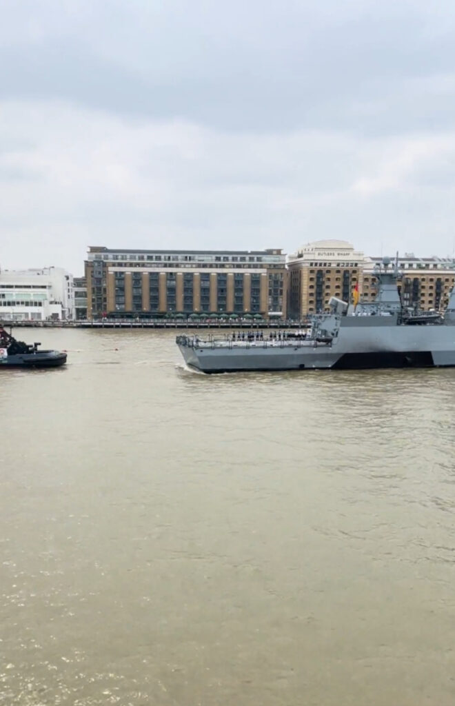 The battleship was towed along the river by a smaller civilian vessel.