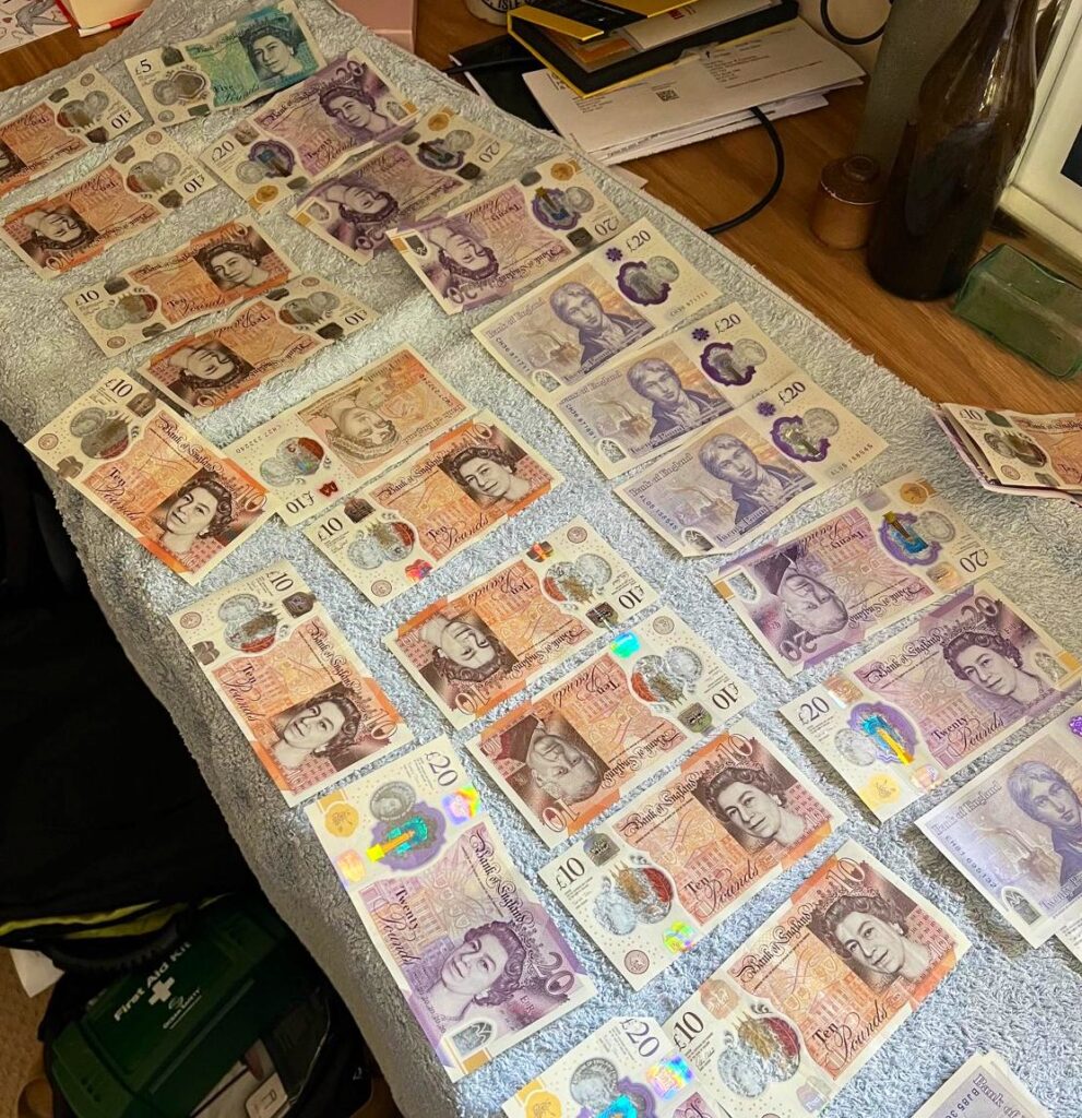 An image of British bank notes, mostly £10 and £20 notes with one £5 note, lying individually on a grey towel on top of a wooden table.