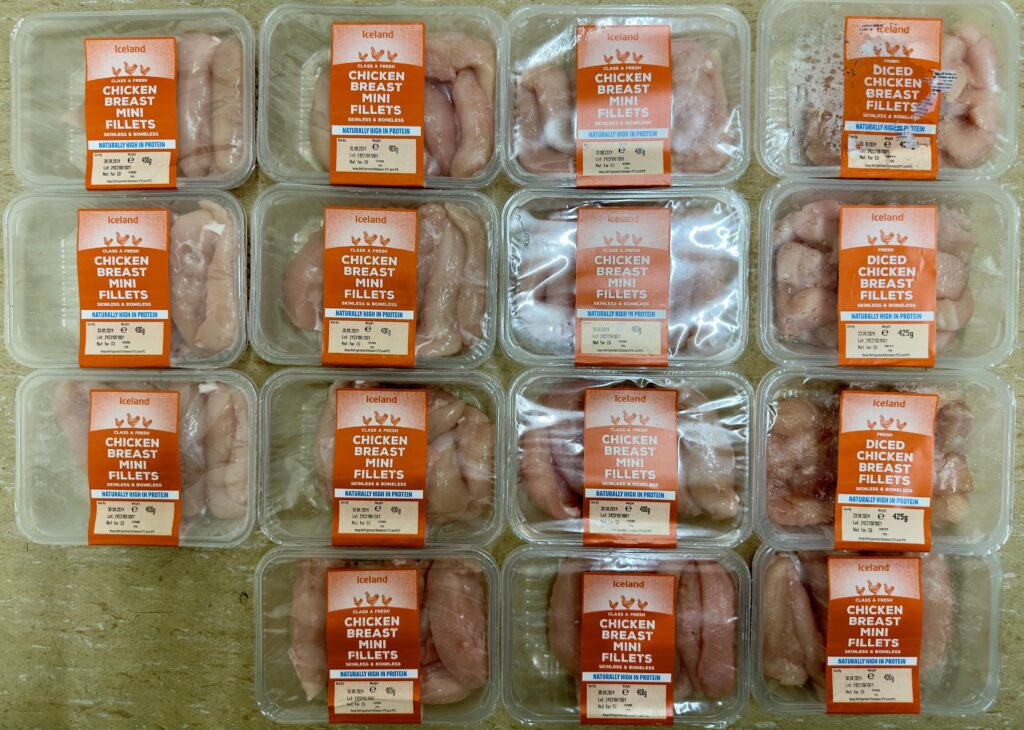 An image of 12 packets of chicken breast mini fillets and 3 packets of diced chicken breast fillets, all from the shop Iceland, in plastic trays with orange labels with white writing.