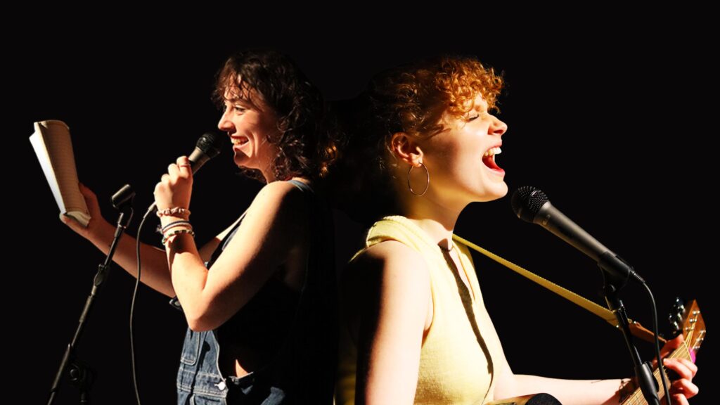 Two young women standing back to back with a black background. The girl on the left has curly dark hair, wears denim dungarees and is smiling as she holds a microphone in her left hand and a book in the other. The girl on the right has curly red hair, wears a yellow top and appears to sing into a microphone while playing a guitar.