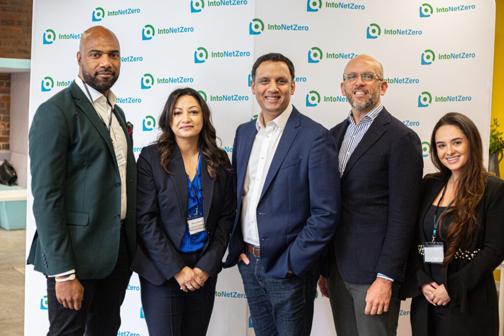 A group of five people dressed in business attire, standing in front of a background featuring a repeating pattern of company name "IntoNetZero".