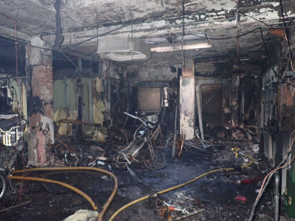 An image of a burned out room with debris and hoses on the floor, and damaged pedicabs scattered around.