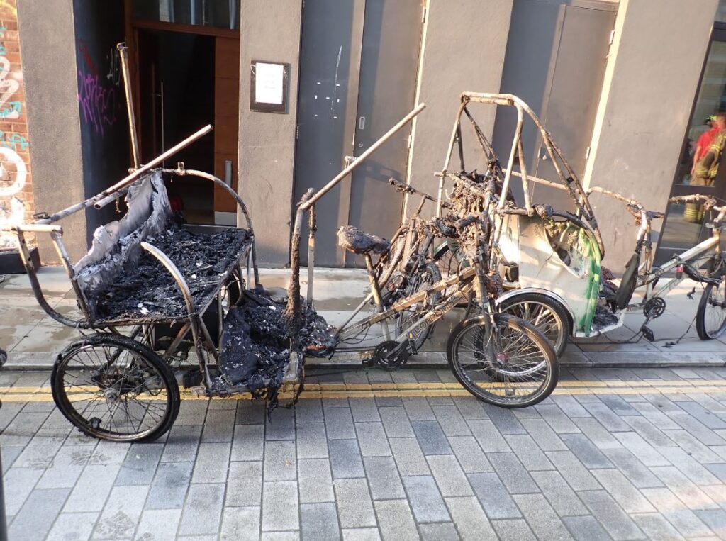 An image of a pedicab badly damaged by fire and reduced to a shell.