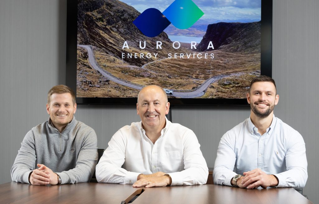 An image of three men sitting at a desk in front of a screen reading: "Aurora Energy Services".