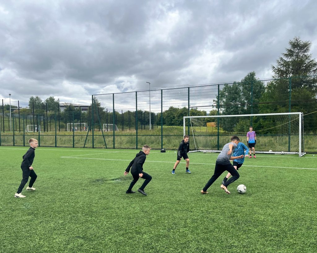 An image of children playing football on an outdoor pitch.