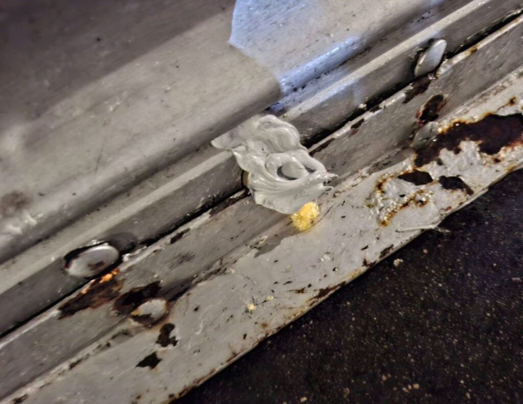 An image of a metal shutter, its lock covered in white filler.