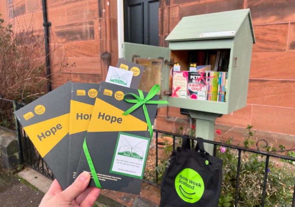 An image of three thin books held up in front of a green wooden box holding more books.