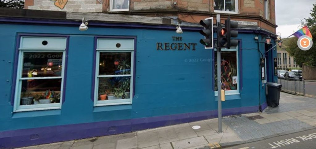 An image of a blue and purple shop front on an old building, with a sign reading: "The Regent". A Pride flag flies from a pole above the door.