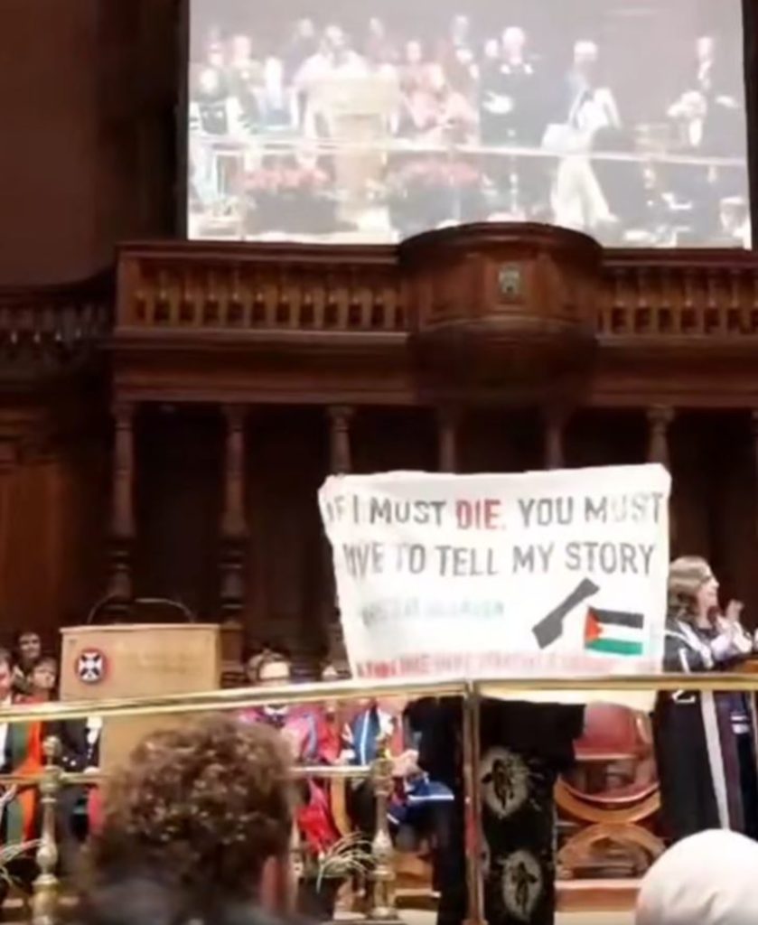 An image of a person on a stage, holding up a banner which obscures most of their body.