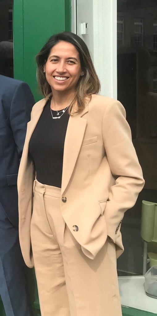 An image of a dark-haired woman wearing a beige trouser suit.