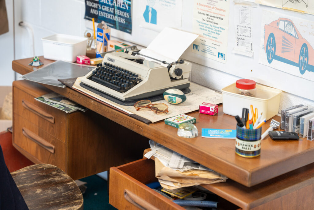 An image of a cluttered desk with a white typewriter in the middle.