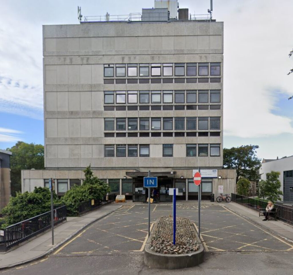 An image of a tall grey building with windows covering two-thirds of its front.