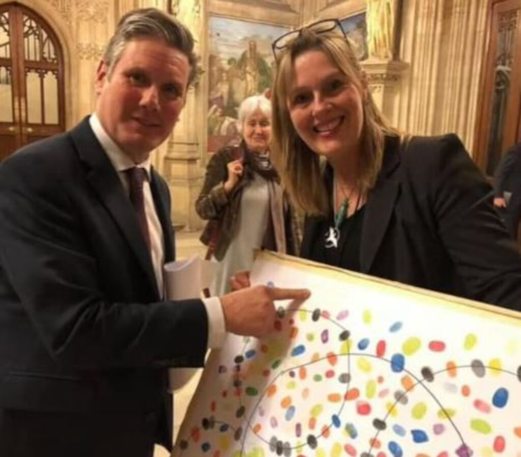 An image of a man and woman holding a white canvas printed with colourful fingerprints.