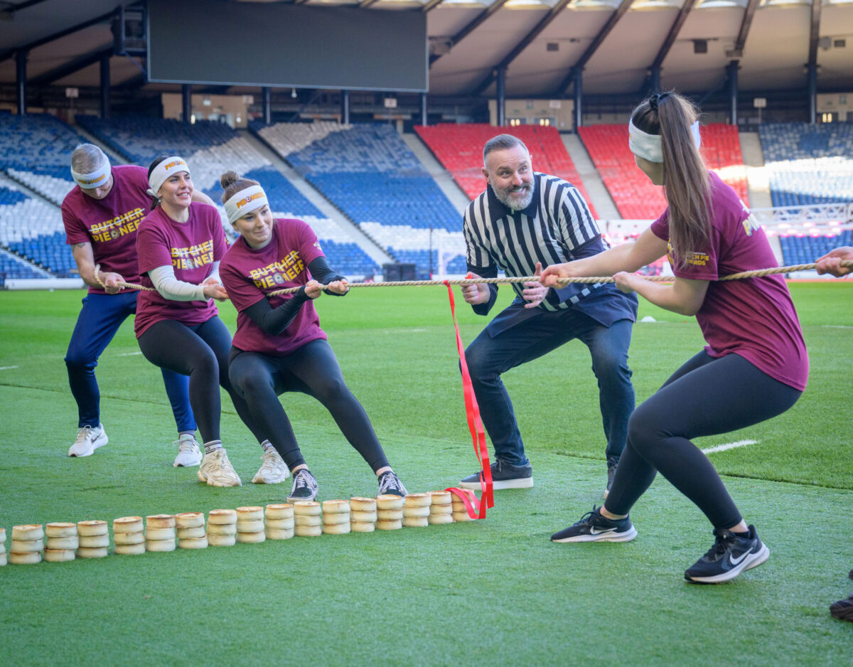 A picture of Kris Boyd referreeing a tug of war competition against (L-R) the Scottish Bakers and the Scotch Butchers Club.