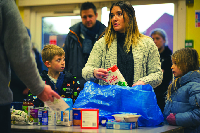 A woman bagging up groceries with children.